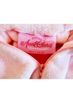 The Aunt Clara's Creations label on pink bunny pajamas says: warm and fuzzy, Aunt Clara's Creations, Sewn in the USA